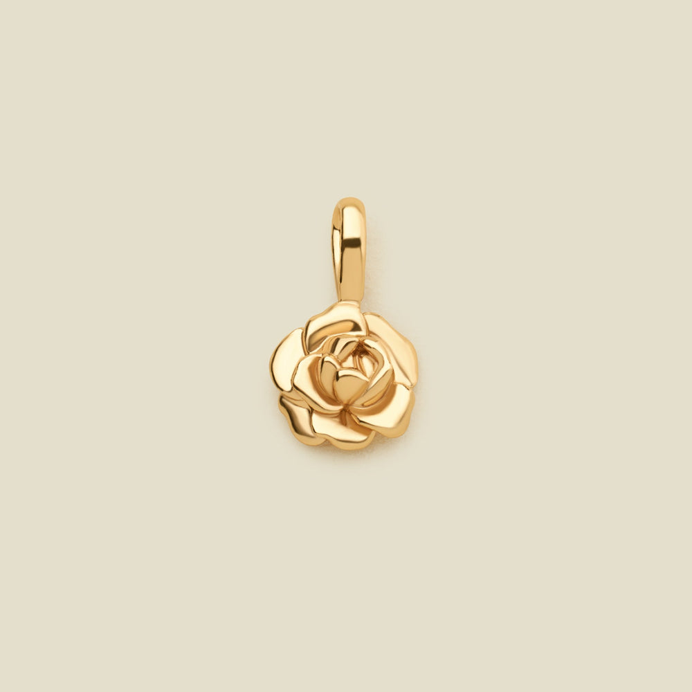 A polished gold peony flower charm pendant with a top loop, centered on a solid light beige background.