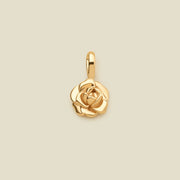 A polished gold peony flower charm pendant with a top loop, centered on a solid light beige background.