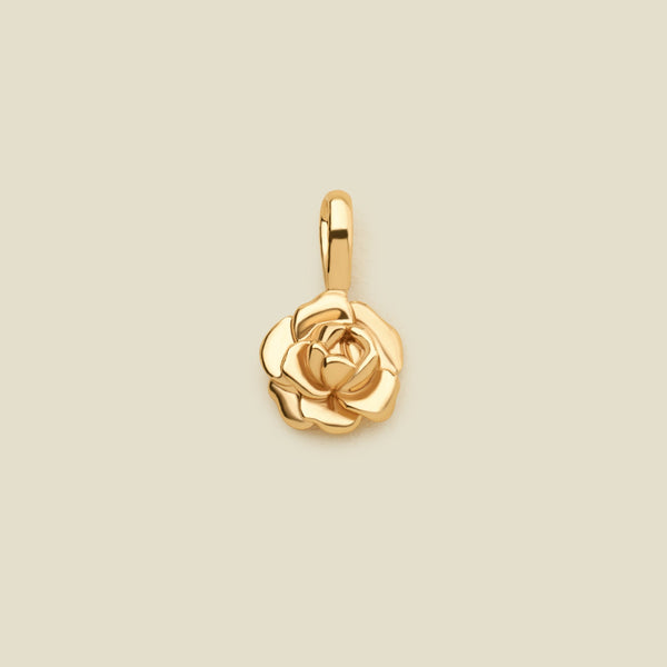A polished gold peony flower charm pendant with a top loop, centered on a solid light beige background.