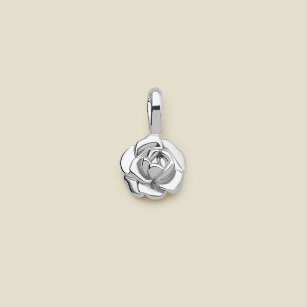 A small polished silver peony flower charm, shown on a solid light beige background.
