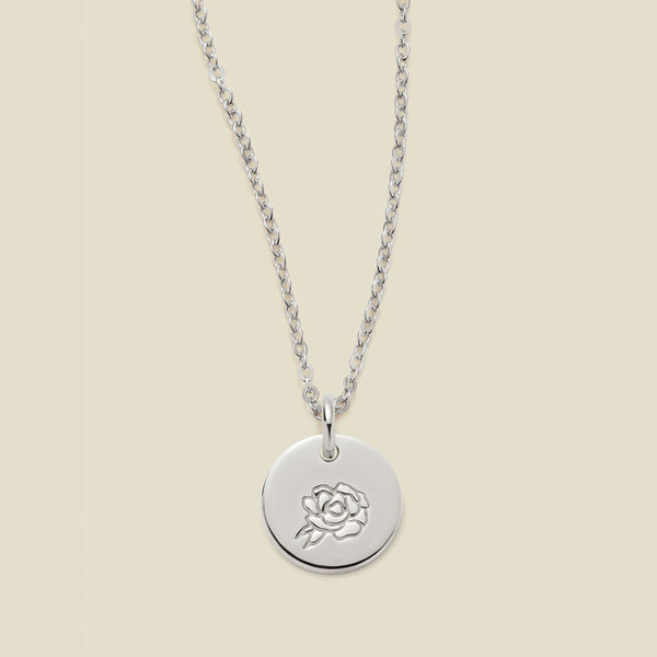 A silver chain necklace with a round silver disc pendant featuring an engraved peony flower design, displayed against a solid light beige background.