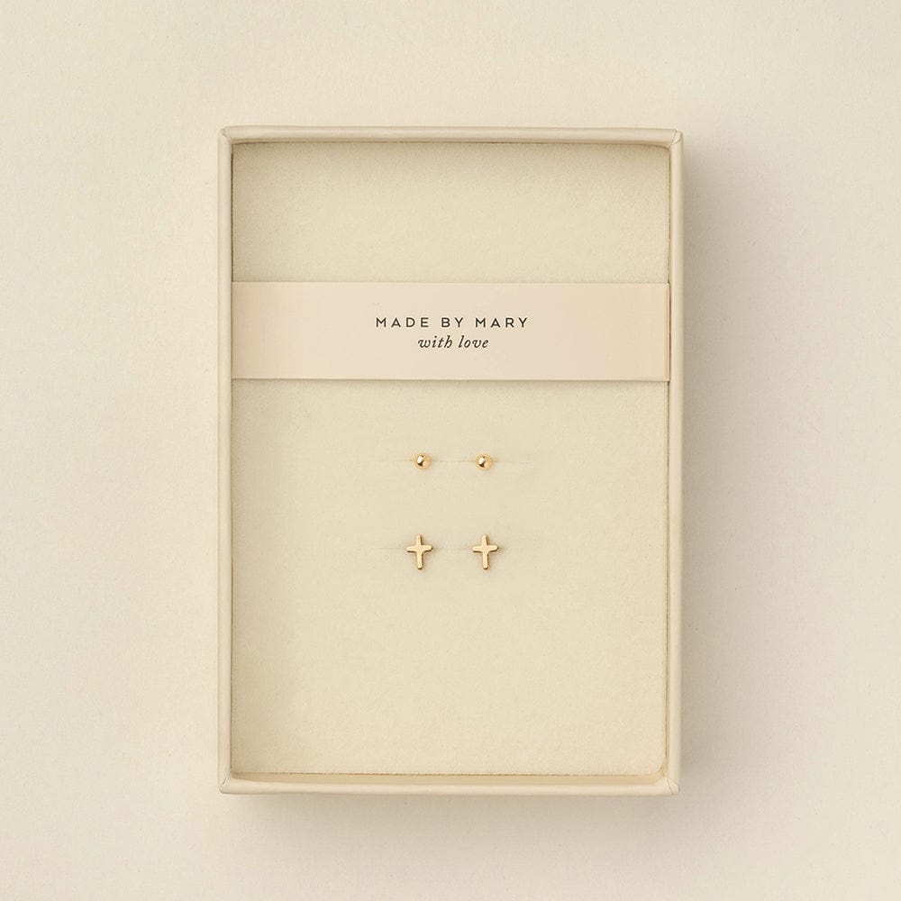Two pairs of gold stud earrings displayed inside a cream-colored jewelry box. One earring is a small round dot, and the other is a small cross.