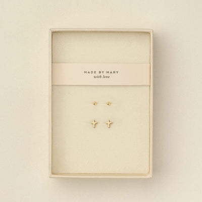 Two pairs of gold stud earrings displayed inside a cream-colored jewelry box. One earring is a small round dot, and the other is a small cross.