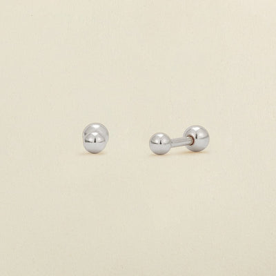 A pair of round silver bead stud earrings with round ball backings, shown against a solid light beige background.