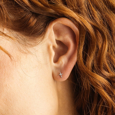 A woman's ear wearing a small silver cross stud.