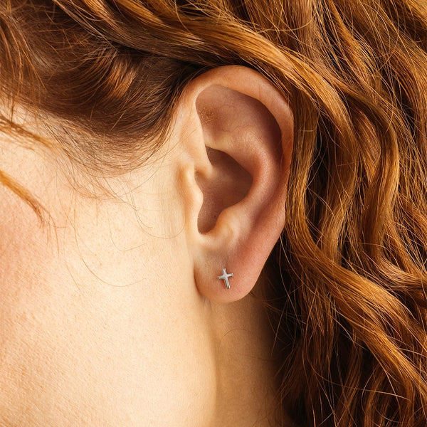 A woman's ear wearing a small silver cross stud.