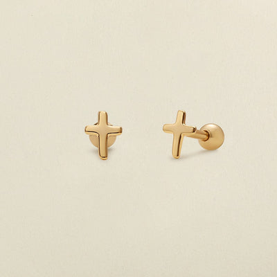 A pair of minimalistic gold cross studs with round ball backings, shown on a solid light beige background.