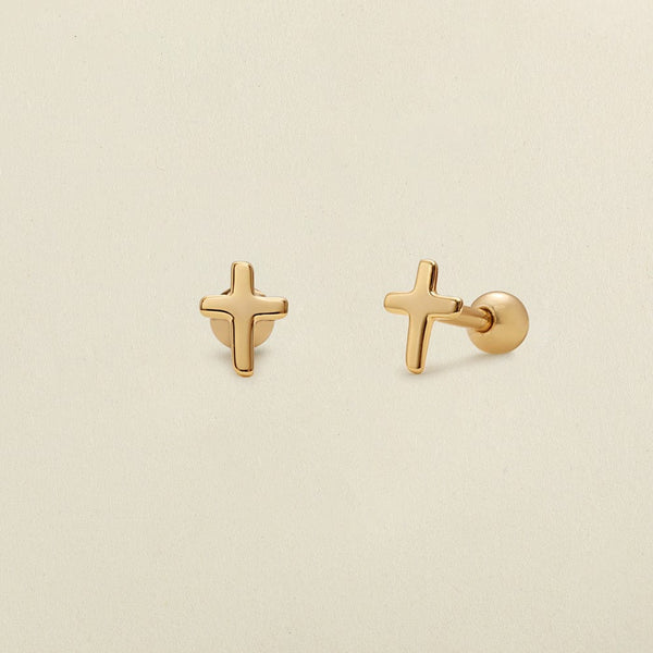 A pair of minimalistic gold cross studs with round ball backings, shown on a solid light beige background.