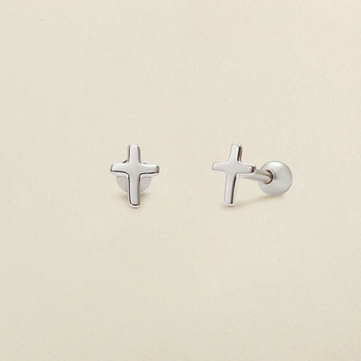 A pair of minimalistic silver cross stud earrings with round ball backings, shown on a solid light beige background.