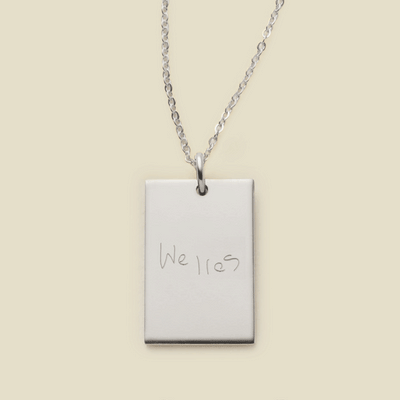 A delicate silver chain necklace with a rectangular silver pendant engraved with handwritten script.