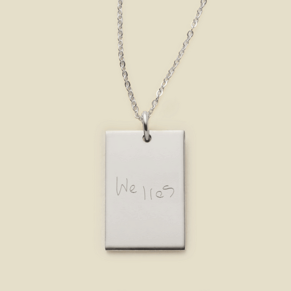 A delicate silver chain necklace with a rectangular silver pendant engraved with handwritten script.