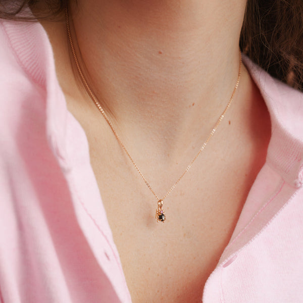 A close-up of a person's chest wearing a pink knit top and a gold pendant chain and a gold spider charm with a large black stone and pink accent stone on the top.