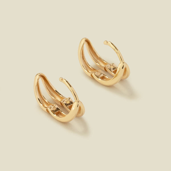A pair of gold huggie hoop earrings shown from the top with the hinge latch open, set on a solid light beige surface.