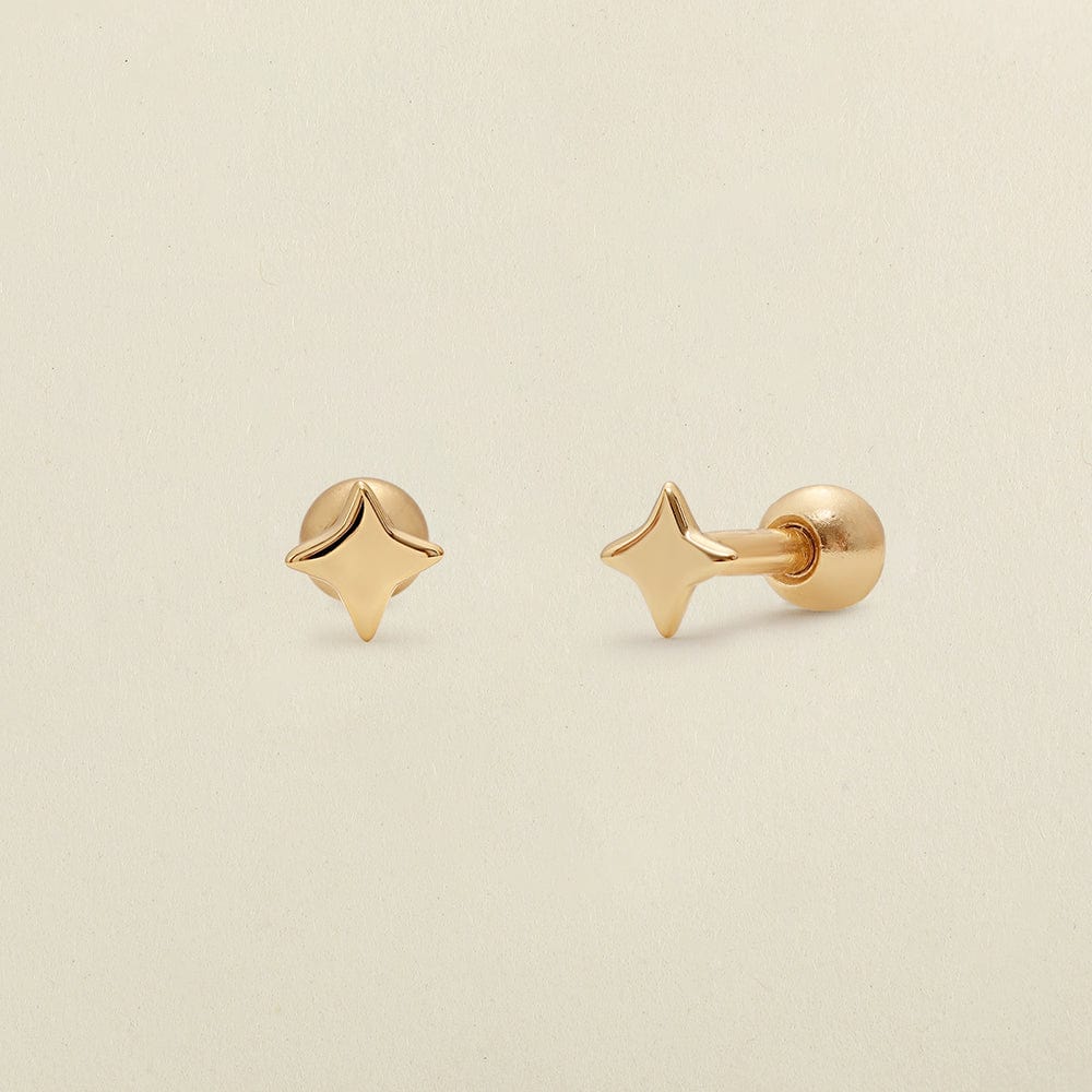 A pair of gold four-point star-shaped stud earrings shown on a clean, light beige textured background.