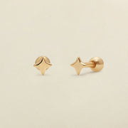 A pair of gold four-point star-shaped stud earrings shown on a clean, light beige textured background.