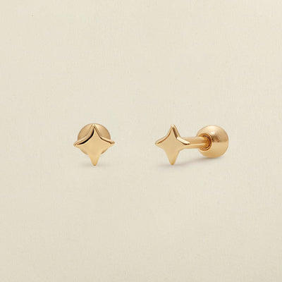 A pair of gold four-point star-shaped stud earrings shown on a clean, light beige textured background.