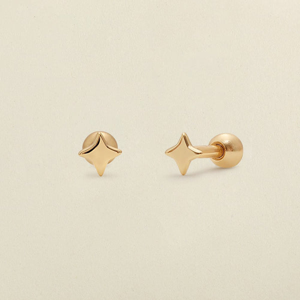 A pair of gold four-point star-shaped stud earrings shown on a clean, light beige textured background.