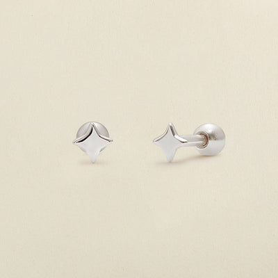 A pair of silver four-point star-shaped stud earrings shown on a clean, light beige textured background.