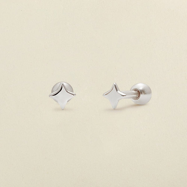 A pair of silver four-point star-shaped stud earrings shown on a clean, light beige textured background.