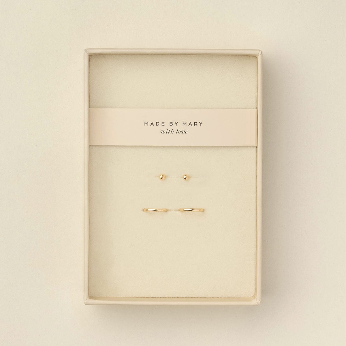 A pair of delicate gold ball stud earrings and matching thin gold hoops displayed in a cream-colored presentation box with a card that reads 'MADE BY MARY with love'.