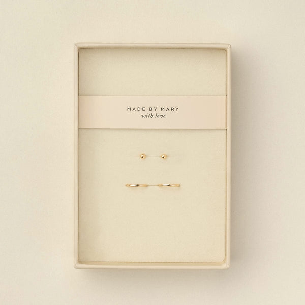 A pair of delicate gold ball stud earrings and matching thin gold hoops displayed in a cream-colored presentation box with a card that reads 'MADE BY MARY with love'.