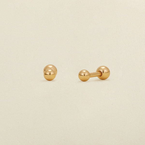 A pair of gold round bead stud earrings with round ball backings, shown on a solid beige background.