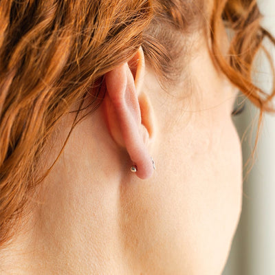 The back of a person's ear, showing a gold round ball backing for an earring.