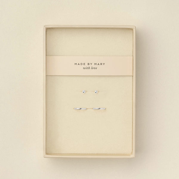 A pair of delicate silver ball stud earrings and matching thin silver hoops displayed in a cream-colored presentation box with a card that reads 'MADE BY MARY with love'.