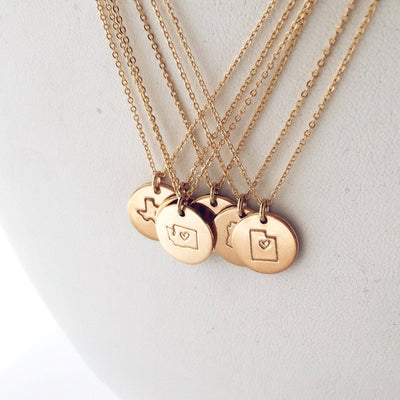 Five gold pendant chain necklaces with round disc charms, each engraved with the outline of a state with a heart in the center.