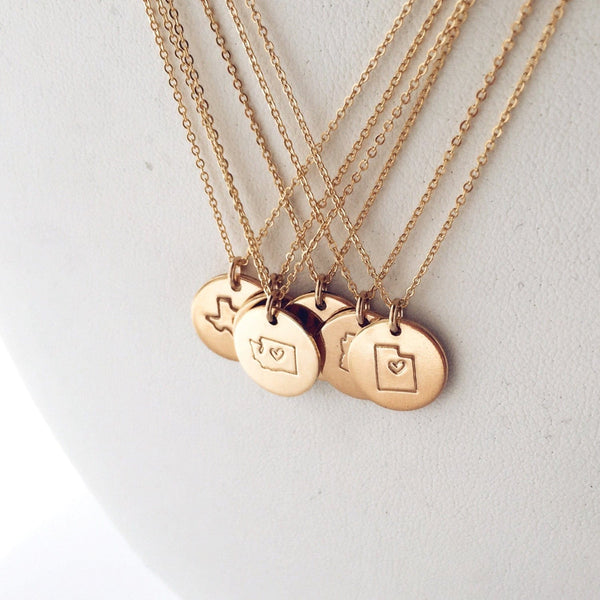 Five gold pendant chain necklaces with round disc charms, each engraved with the outline of a state with a heart in the center.