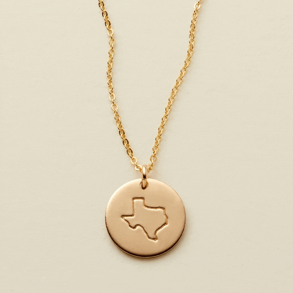 A gif of a delicate gold pendant chain necklace with a round disc charm, changing engravings between outlines of different states.