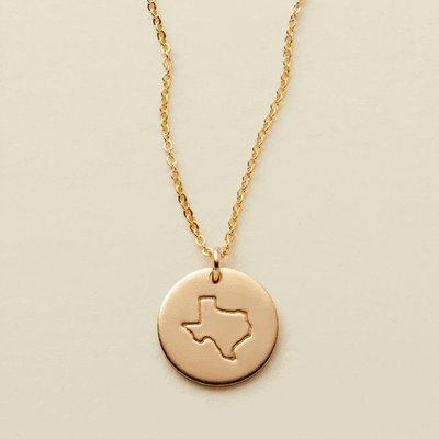 A gif of a delicate gold pendant chain necklace with a round disc charm, changing engravings between outlines of different states.