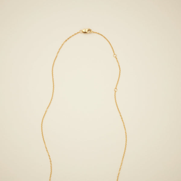  The end of a gold pendant chain necklace, showcasing a gold lobster clasp and round rings that it can attach to, shown on a solid light beige surface.