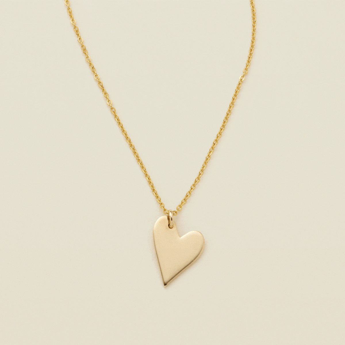 A gif of a delicate gold pendant chain necklace with a flat gold heart charm, starting blank then being engraved with the letter 'M'. From there, multiple smaller engraved heart charms are added one by one, each with a different initial.