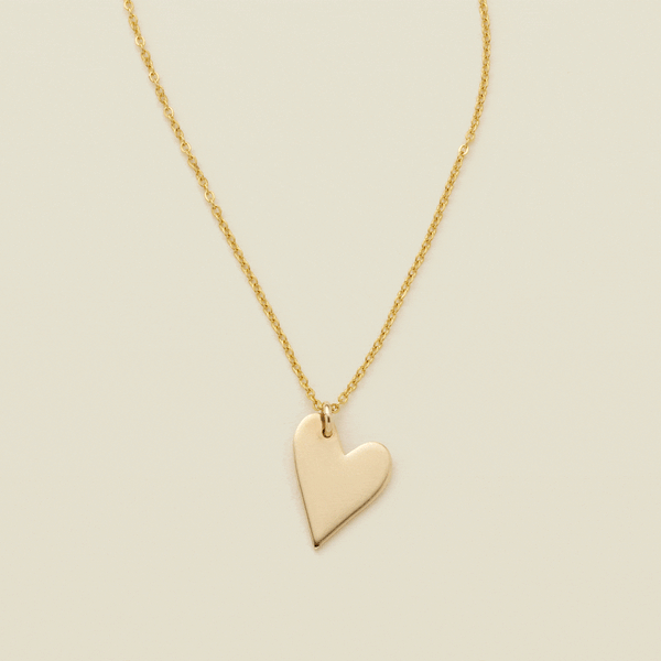 A gif of a delicate gold pendant chain necklace with a flat gold heart charm, starting blank then being engraved with the letter 'M'. From there, multiple smaller engraved heart charms are added one by one, each with a different initial.