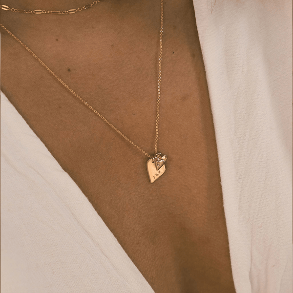 A person wearing a delicate gold pendant chain necklace with a large gold flat heart charms and multiple smaller heart charms.