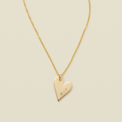 A gift of a delicate gold pendant chain necklace, starting with a large flat heart charm engraved with 'M + T', then adding multiple smaller flat heart charms. Each miniature heart charm is engraved with a single initial.