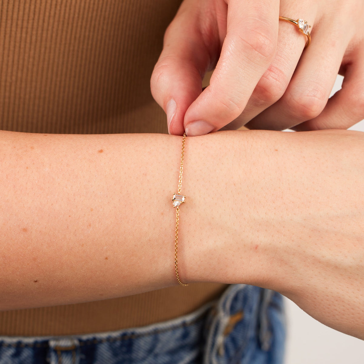 A close-up of a person's wrist wearing a delicate gold chain bracelet with clear baguette and pear gemstones in prong settings.