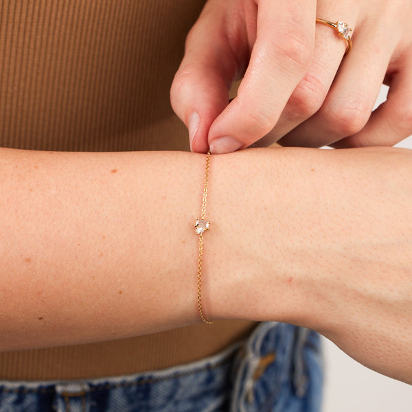 A close-up of a person's wrist wearing a delicate gold chain bracelet with clear baguette and pear gemstones in prong settings.