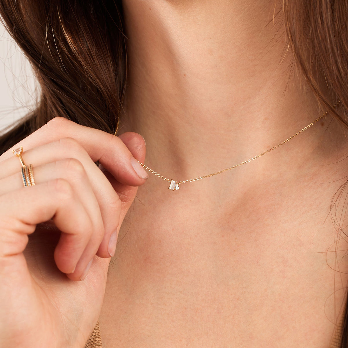 A close-up of a person wearing a delicate gold chain necklace with clear baguette and pear-cut gemstones side-by-side in prong settings in the center.