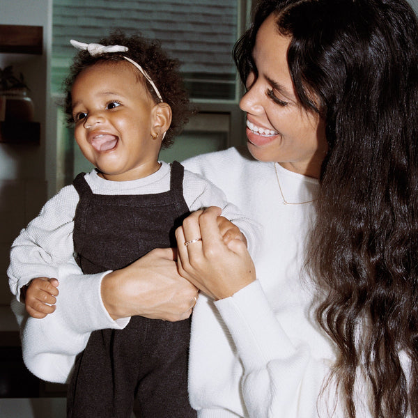 A mother holding her happy small child, wearing matching white long sleeve tops and smiling at her lovingly.