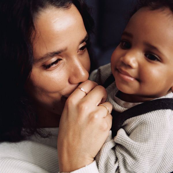 A close-up of a mother holding a small child, kissing the child's hand and showcasing two gold rings.
