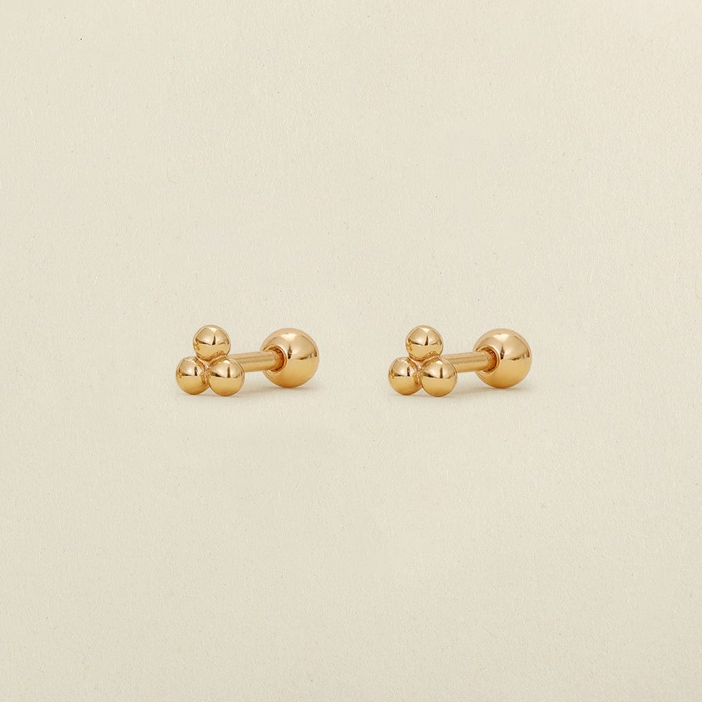 A pair of gold stud earrings with three spherical beads, displayed on a light beige textured background.
